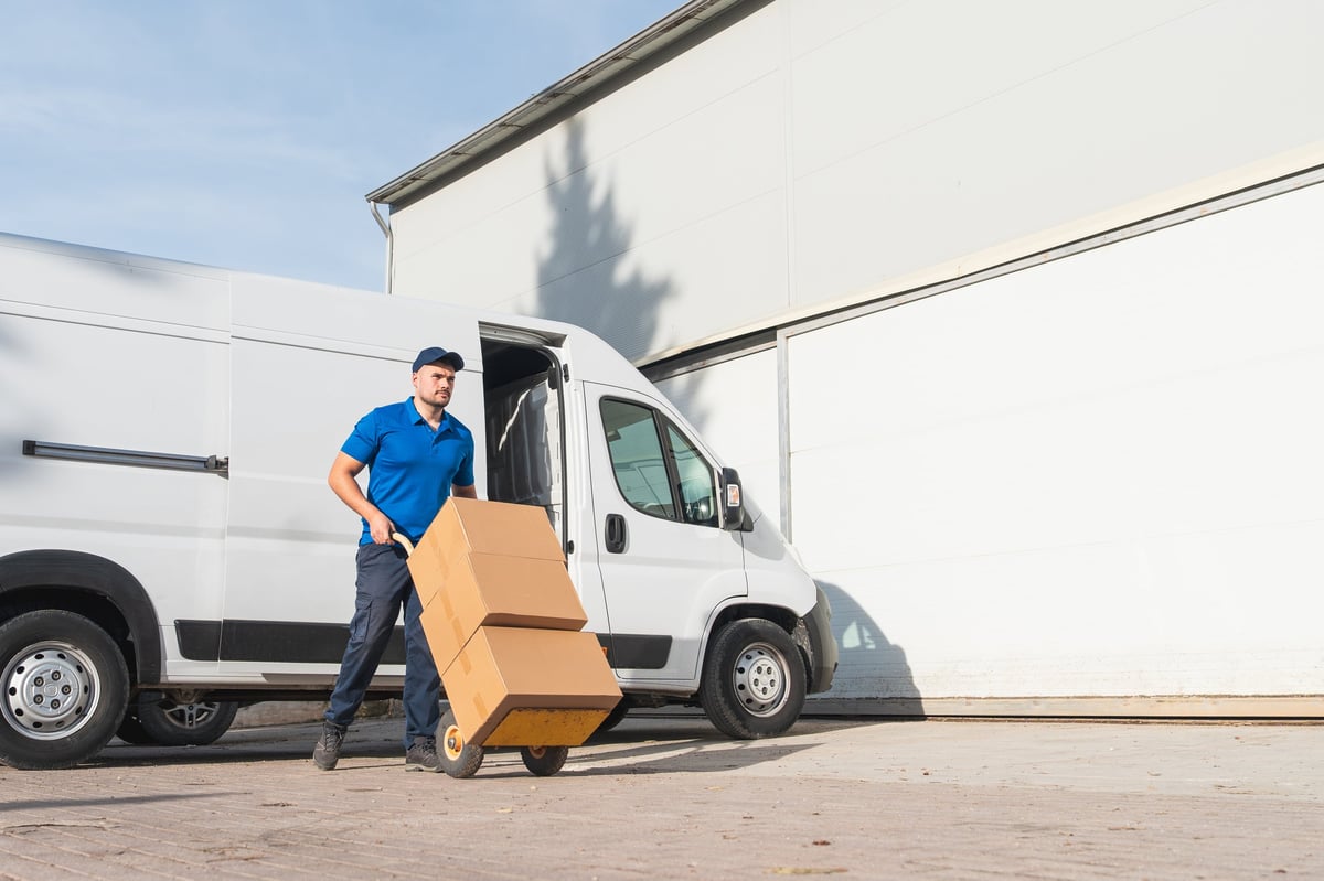 Delivery worker loading boxes beside a white box truck at a warehouse